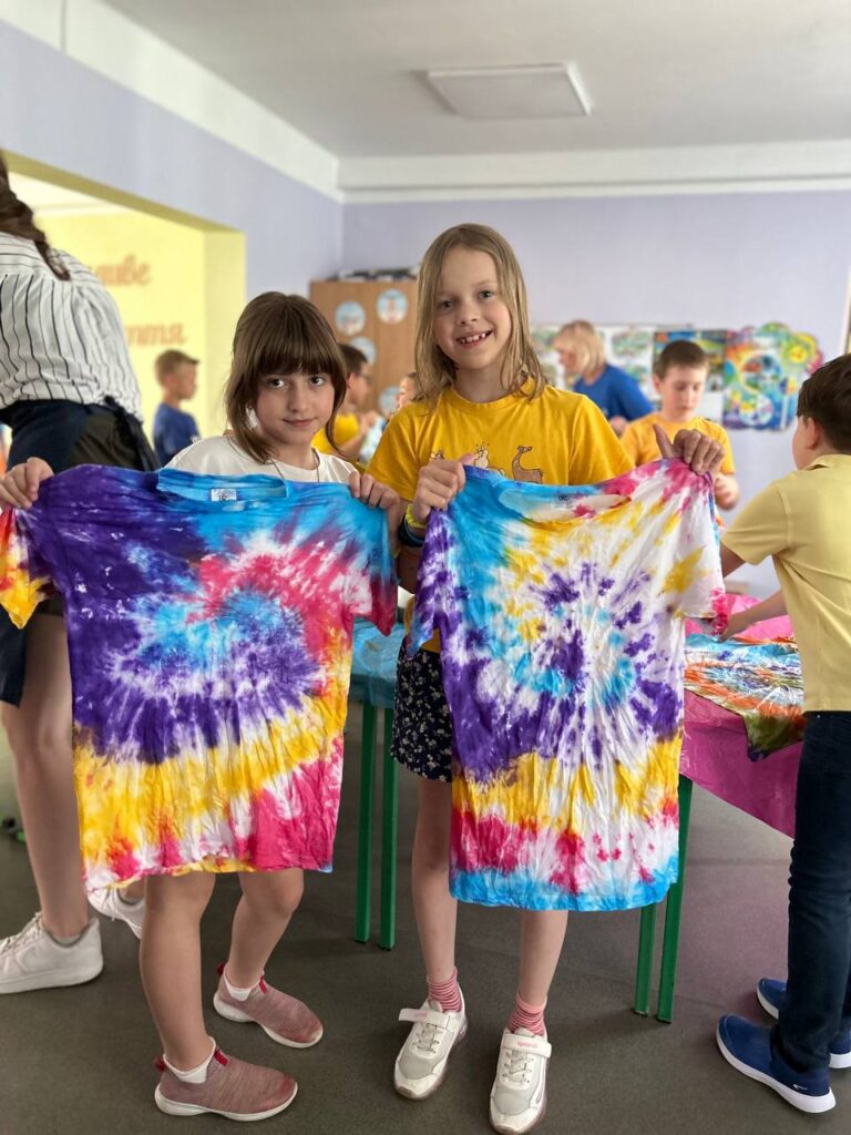 Діти тримають розписані футболки Тай Дай на творчому майстер-класі від Творчої Мозаїки у школі