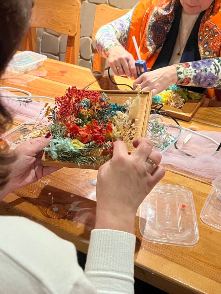 Процес створення картини з сухоцвітами: розміщення квітів і трав у рамці під керівництвом майстрині.