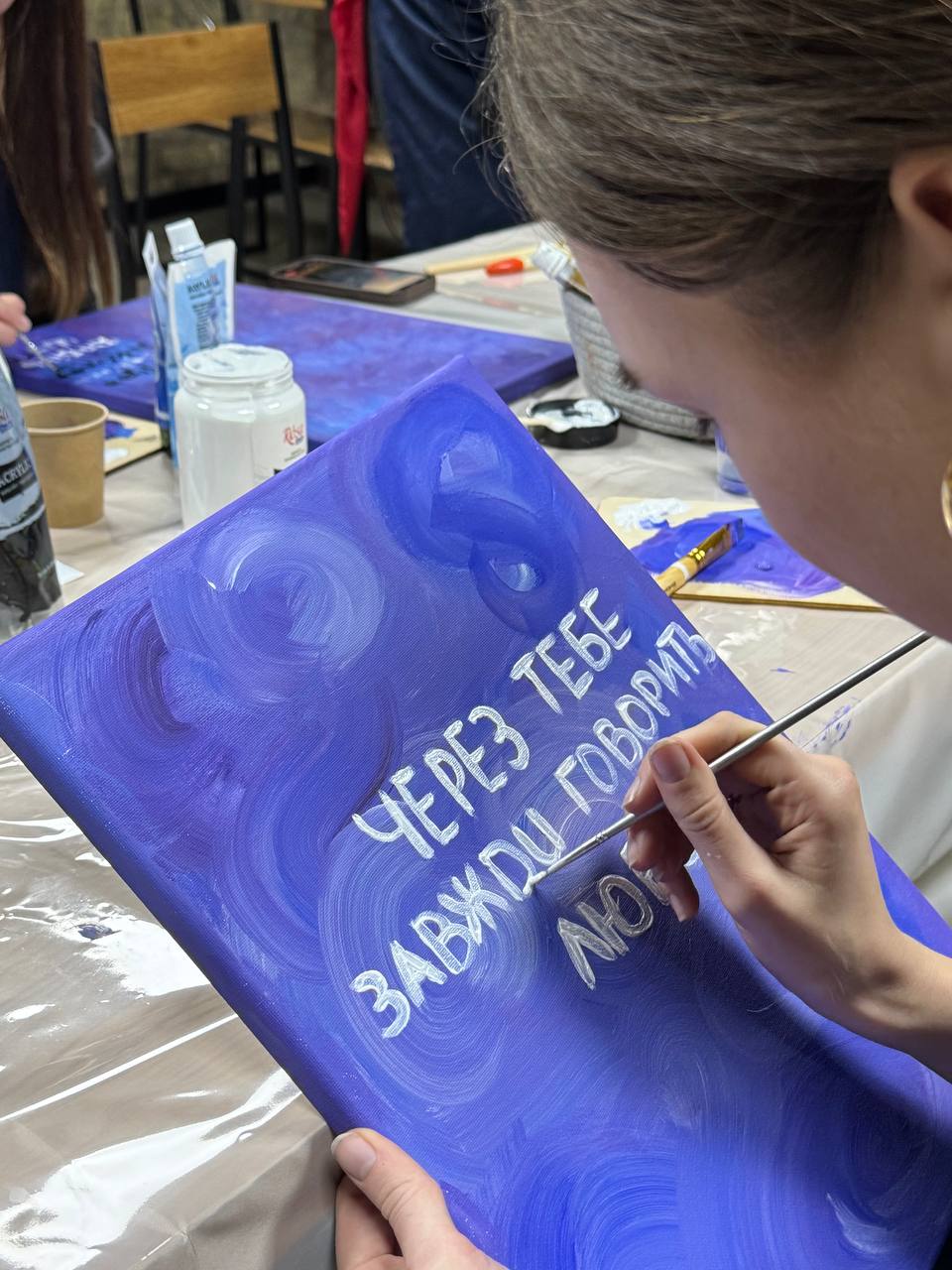 Учасниця розписує картину з афірмацією на полотні акриловими фарбами під час творчого майстер-класу «Творчої Мозаїки».