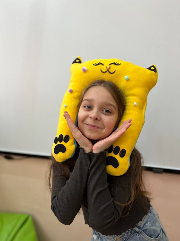 Дівчинка тримає жовту тревел подушку-котика, зроблену на майстер-класі для дітей у Києві.