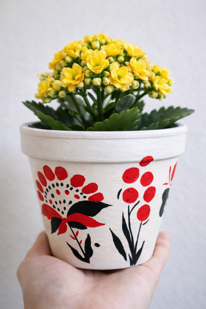 Розписаний керамічний горщик з жовтим каланхоє в руках — майстер-клас з розпису горщиків і висадки квітів